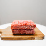 Two RawFedK9 Pure Meat patties placed on a cutting board, showcasing high-quality, single-protein raw dog food ready to serve.