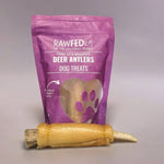 Pork skin wrapped deer antler chew laying in front of its RawFedK9 product bag on a neutral background.