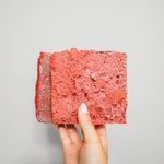 Hand holding RawFedK9 PMR patties against a white background, highlighting the texture and quality of balanced raw dog food made with muscle meat, bone, and organ.