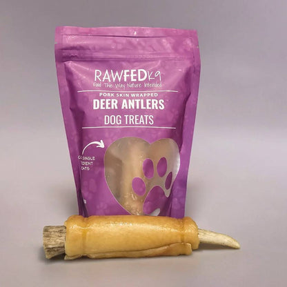 Pork skin wrapped deer antler chew laying in front of its RawFedK9 product bag on a neutral background.