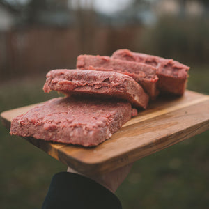 RawFedK9 PMR patties arranged on a cutting board, showcasing balanced, biologically appropriate raw meals made from muscle meat, bone, and organ.